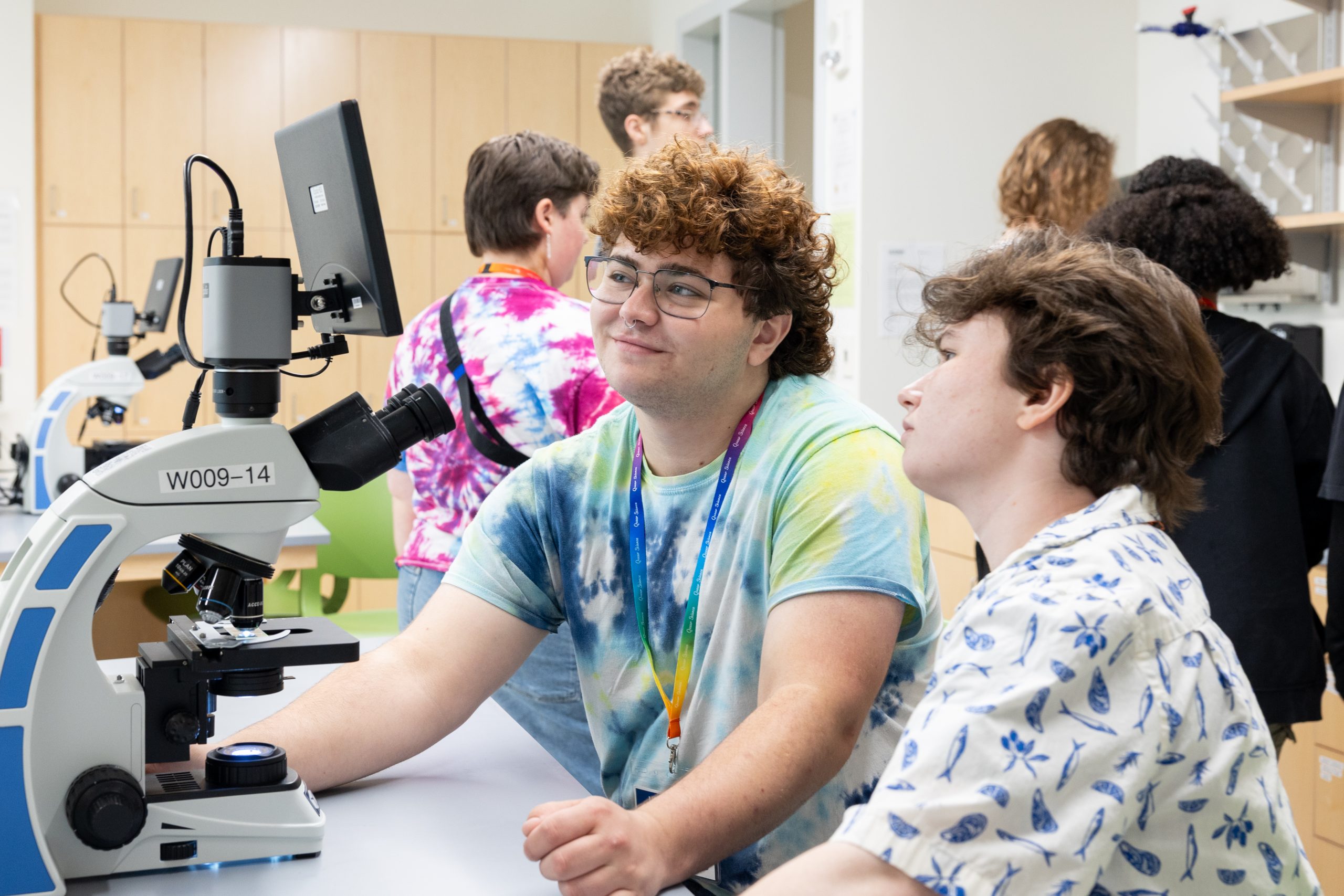 Two students in lab, dressed casually, looking at microscope
